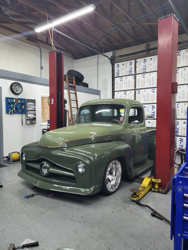 A classic green Ford pickup up on the lift inside the shop
